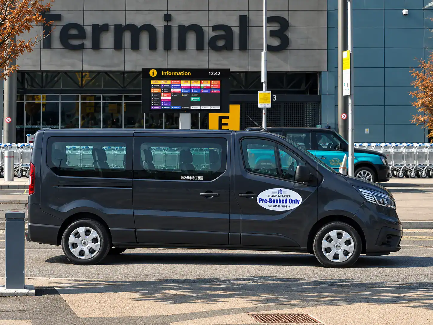 Airport transfer Downham Market – G and M Taxis dark grey Renault minibus parked outside an airport Terminal 3 entrance.