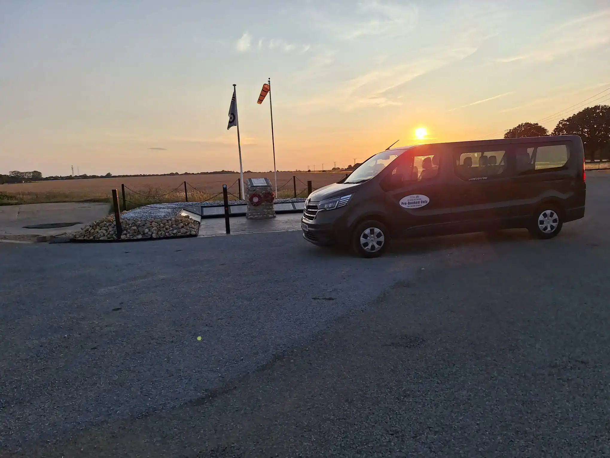 Dark blue G and M Taxis minibus parked beside open Norfolk countryside at sunset, providing wedding cars and event transport in Downham Market.